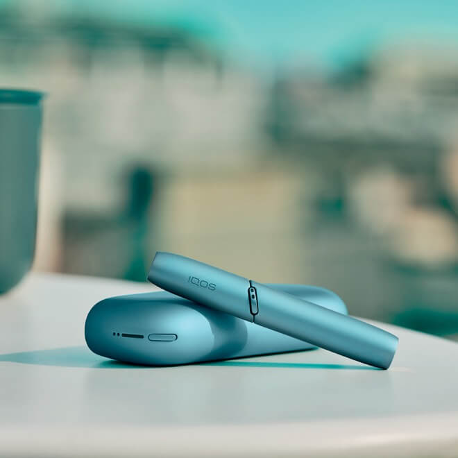 Man with paint on hands holding a turquoise IQOS Originals One heated tobacco device.  